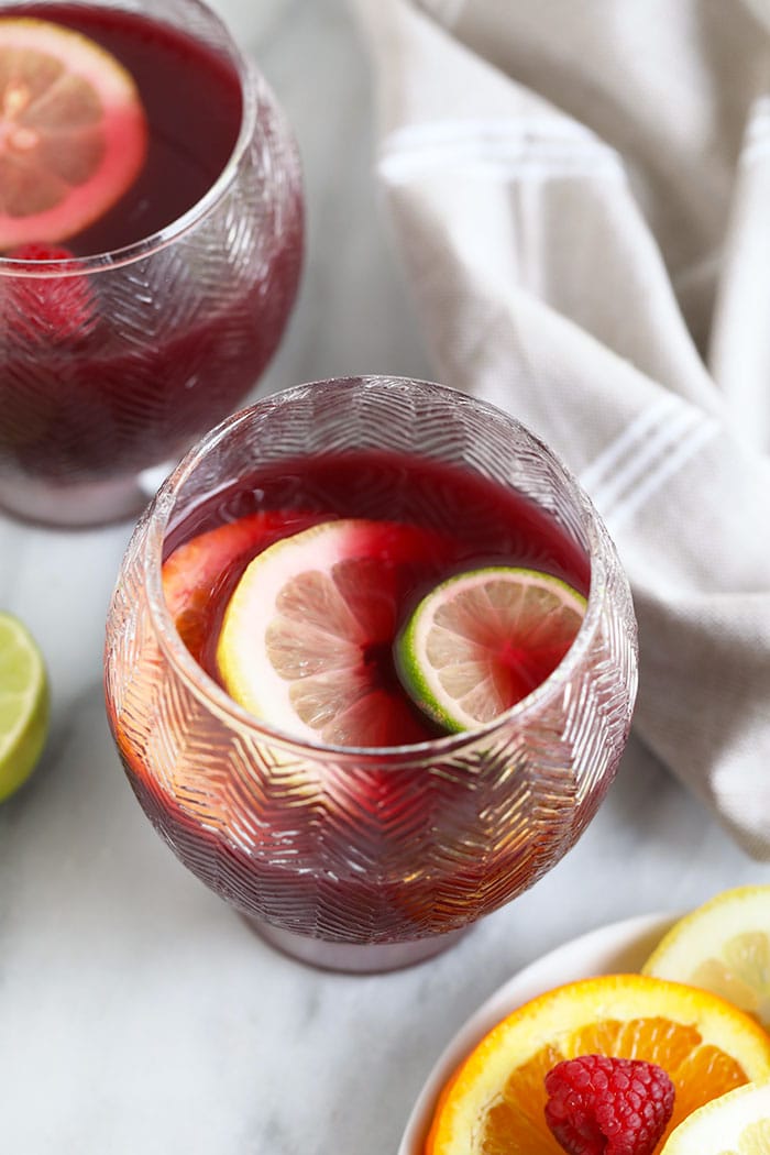 We're sharing an easy sangria recipe that you are going to love! Red wine sangria is made with your favorite Spanish red, orange juice, rum, and tons of sliced citrus. sangria in cup with sliced fruit