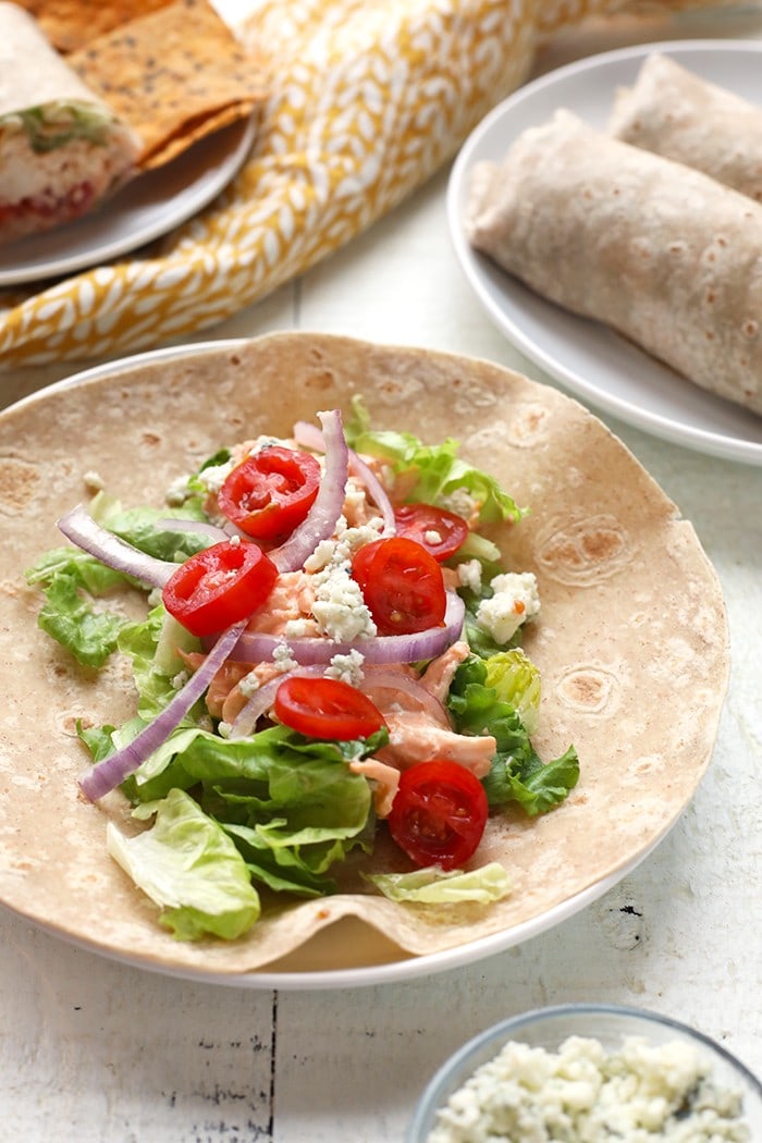 healthy chicken wrap ingredients on tortilla including tomatoes, onion and buffalo chicken