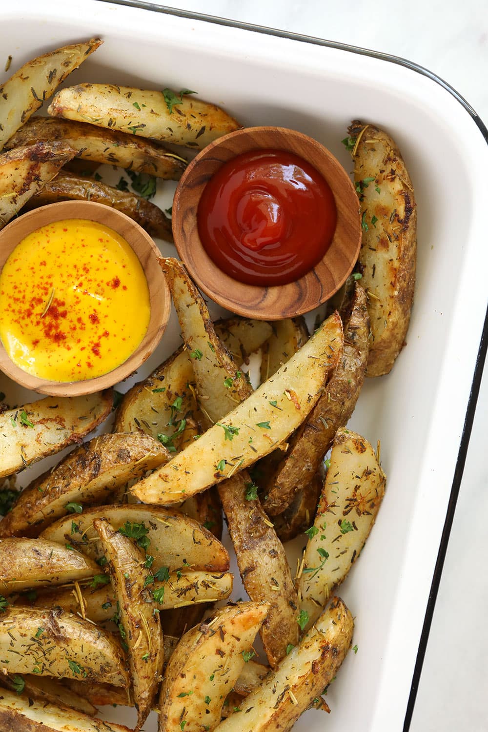 Potato wedges in a pan with ketchup and mustard.