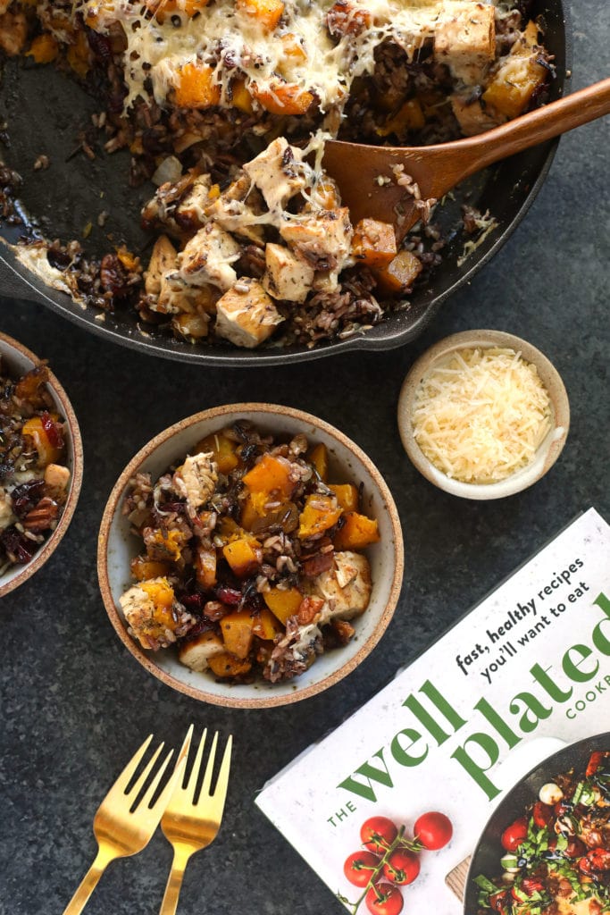 Straight from The Well Plated Cookbook, this Butternut Squash Wild Rice Casserole is the ultimate Fall dish! butternut squash wild rice casserole in a cast iron pan being scooped with a wooden spoon