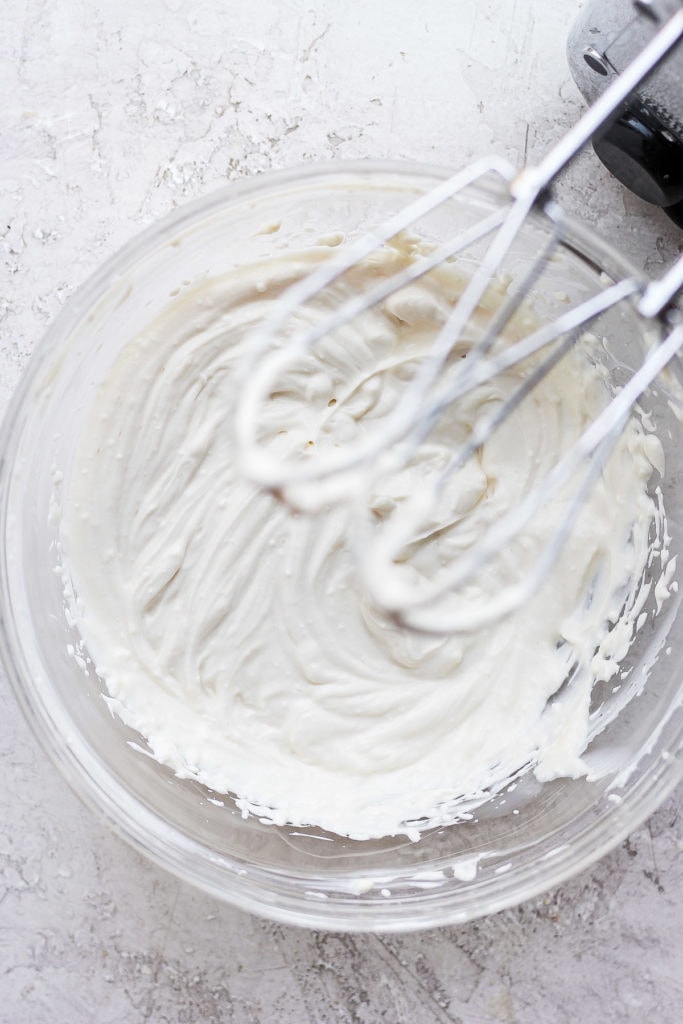 This Greek yogurt cream cheese frosting is the most delicious healthy cream cheese frosting we've ever had! cream cheese frosting with hand mixer in bowl