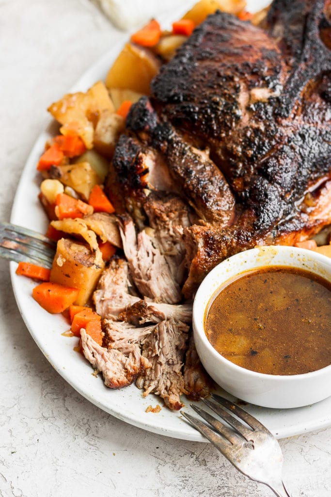 The best oven baked pork roast recipe made with tender potatoes and carrots served with a delicious savory gravy. Make this for dinner tonight! perfectly cooked pork roast on a serving platter