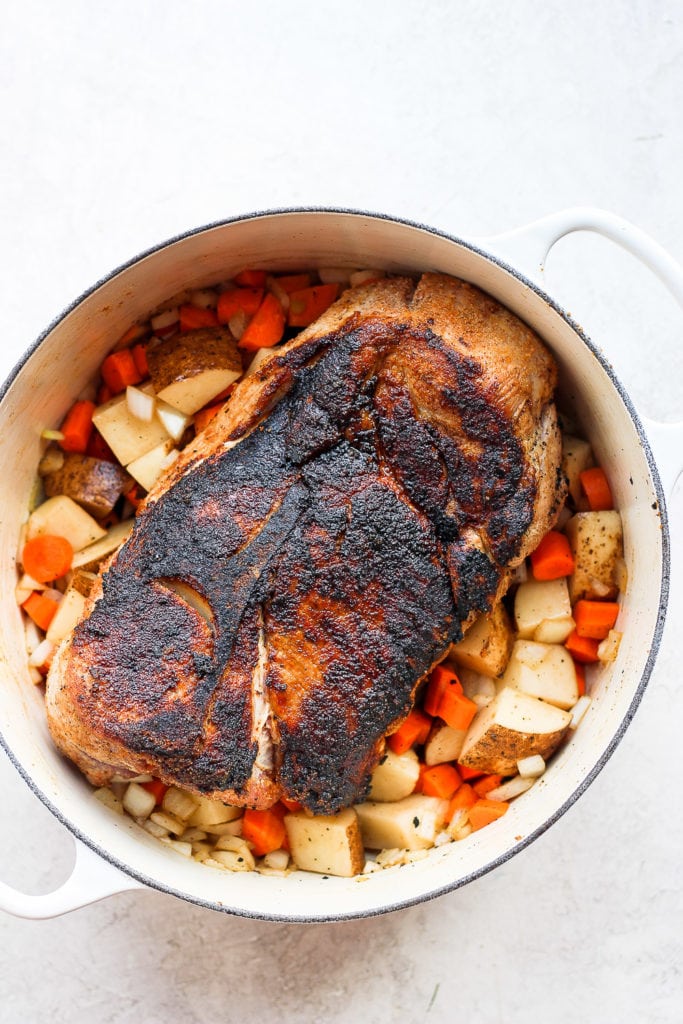 The best oven baked pork roast recipe made with tender potatoes and carrots served with a delicious savory gravy. Make this for dinner tonight! pork shoulder surrounded by veggies and ready to be roasted