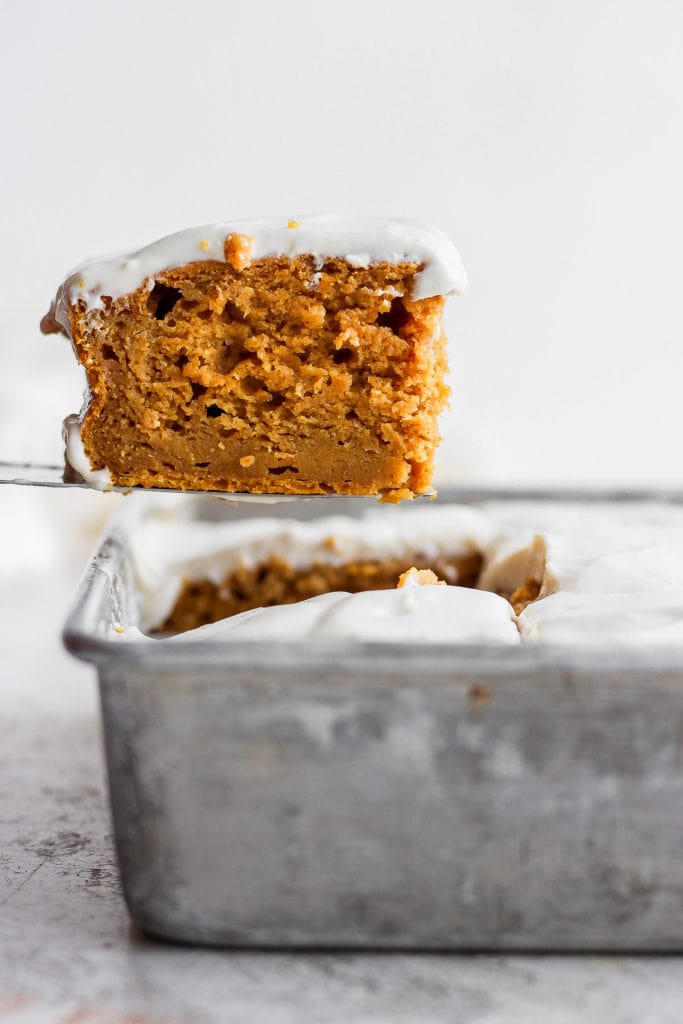 This pumpkin sheet cake is as easy as it is delicious. Packed with simple ingredients and topped with a yummy cream cheese frosting, this dessert can't be beat! slice of pumpkin sheet cake coming out of the pan