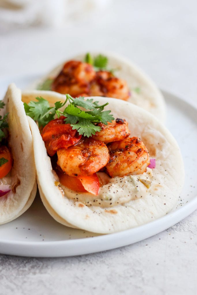 These shrimp tacos are the ultimate easy weeknight meal! With a sweet pepper slaw and an avocado greek yogurt sauce, the flavors of these tacos can't be beat. shrimp tacos in a street taco tortilla looking delicious