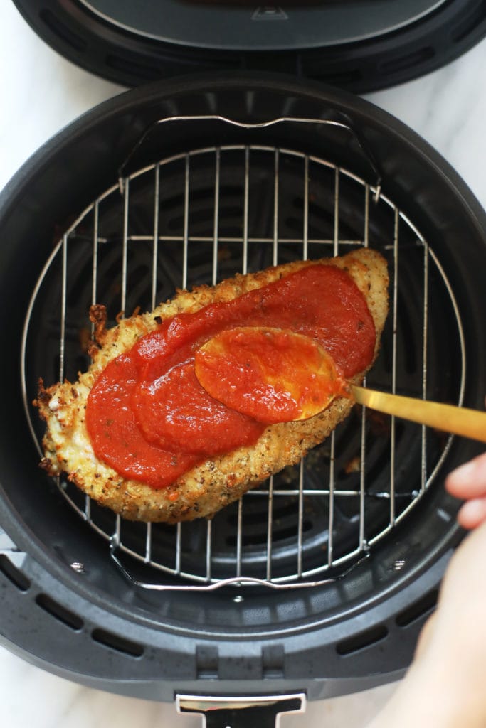This air fryer chicken parmesan takes no time to whip up and only requires 5 main ingredients. Bonus - there is no oil involved! rubbing chicken parmesan with marinara sauce in air fryer