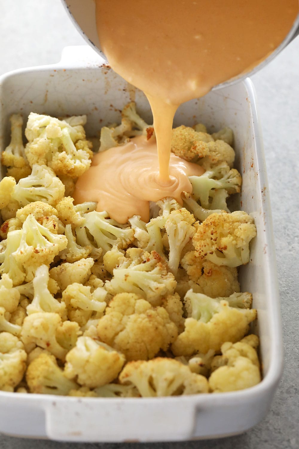 This Three Cheese Cauliflower Mac and Cheese is keto, low carb, and oh so delicious! And did we mention it packs 20g of protein? Yah welcome. cauliflower mac and cheese with the sauce being poured over cauliflower