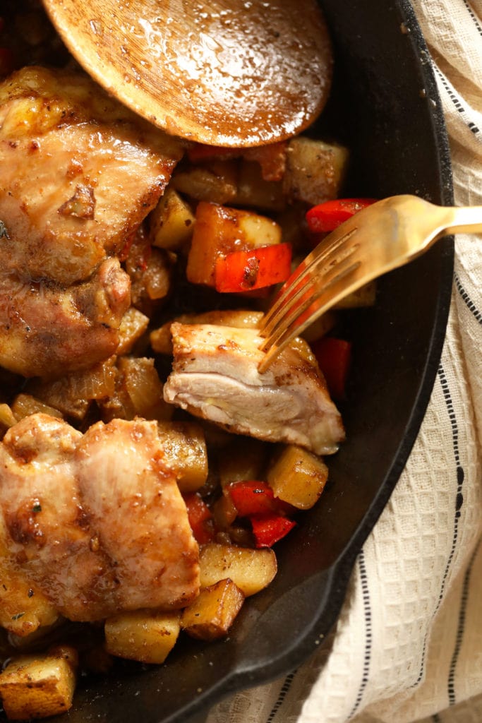 This Skillet Chicken and Potatoes is the perfect easy weeknight meal! With savory fall veggies and deliciously seasoned chicken thighs, this recipe will quickly become a staple in your kitchen! bite of a chicken thigh on a fork ready to eat