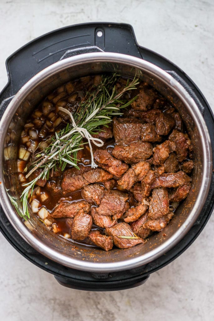This Instant Pot Beef Stew is everything slow roasted stew is, but without the long cook time! Fall apart beef and tons of veggies, plus its ready to eat in under an hour. beef stew in the instant pot with an herb bundle placed on top