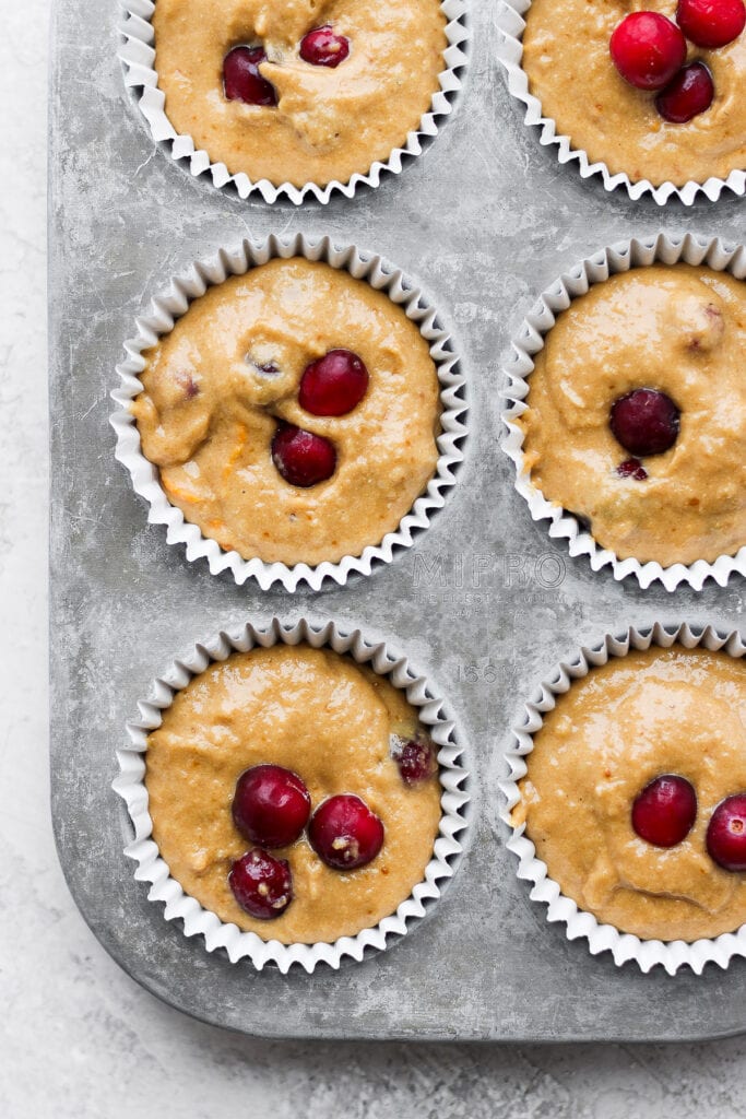 These Cranberry Orange Muffins are bursting with all those seasonal flavors you love! Made from healthy ingredients, including fresh cranberries and orange zest. Enjoy! cranberry orange muffins in a muffin tin, ready to be baked