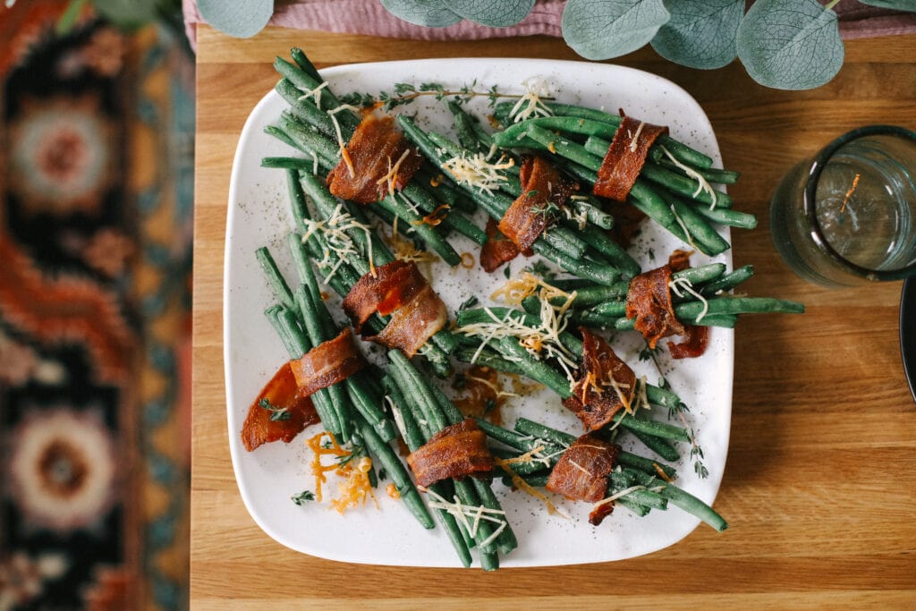 This Thanksgiving appetizer idea is finger-lickin' good. Little bundles of green beans wrapped in bacon and baked to perfection. Yes, please! green beans on plate on table