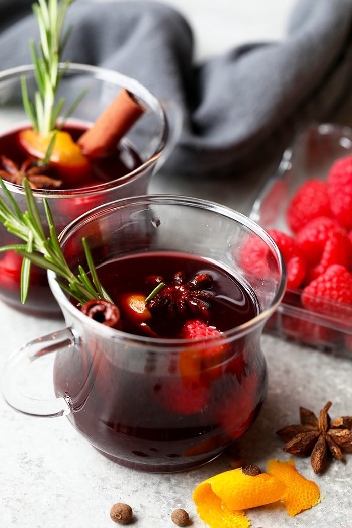 With just a few simple ingredients you can make your guests this delicious, spicy raspberry mulled wine. This raspberry mulled wine recipe is perfect for a cool Fall day or the holidays! festive mulled wine in a mug with rosemary