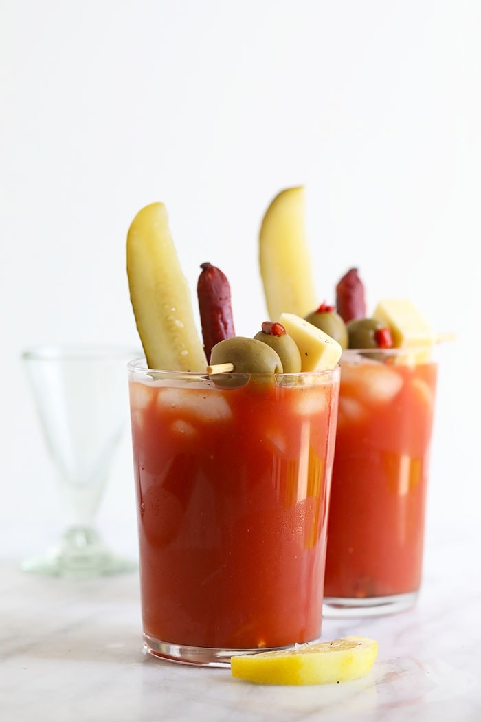 Start your next weekend brunch off with this bloody mary recipe! Forget those store-bought mixes and make this homemade bloody mary recipe in the comfort of your own home. Don’t forget all the meat sticks, cheese, and fermented goodness that goes along with the perfect bloody mary, too! Bloody mary in a glass with pickles, olives, and cheese