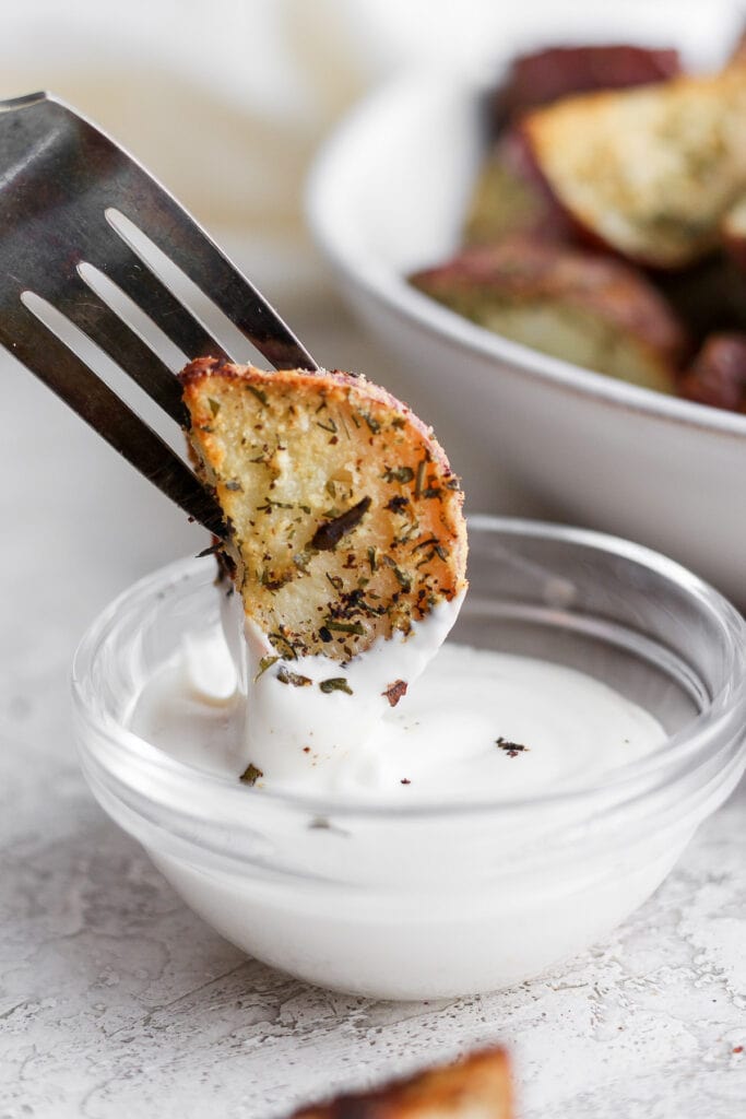 These Ranch Roasted Potatoes are flavor-packed and deliciously crispy! Whip up a batch for the most flavorful side dish. roasted red potato being dipped into ranch dressing