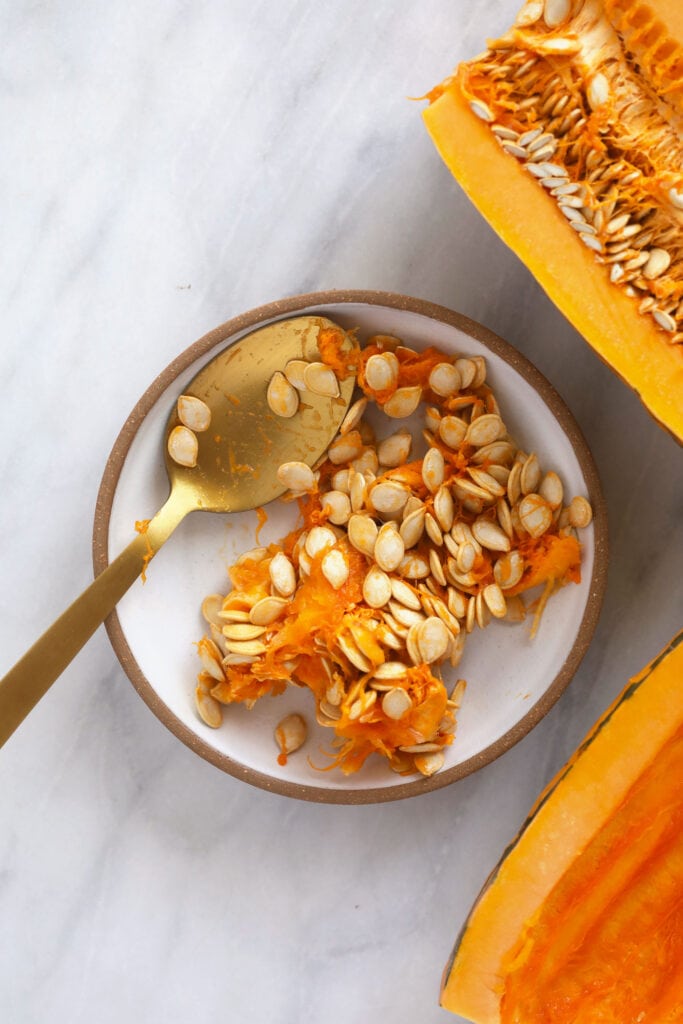 This Easy Roasted Delicata Squash is the perfect pairing to any harvest meal! Enjoy a creme fresh drizzle and the rich savory flavors of delicata squash. No peeling required! delicata squash seeds being scooped out with a spoon