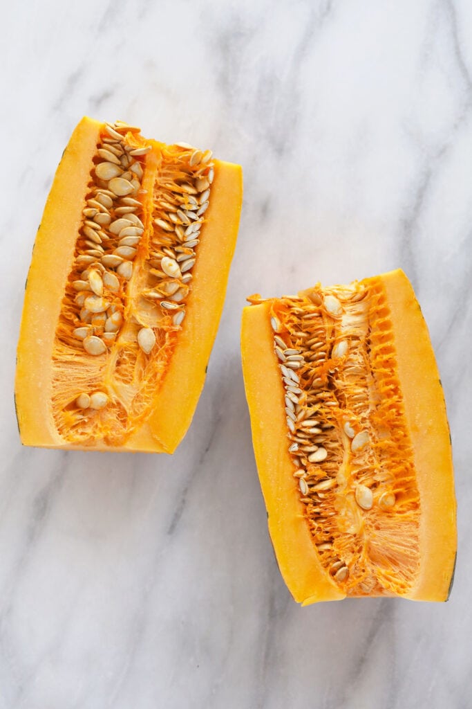 This Easy Roasted Delicata Squash is the perfect pairing to any harvest meal! Enjoy a creme fresh drizzle and the rich savory flavors of delicata squash. No peeling required! delicata squash cut in half with the seeds ready to be removed
