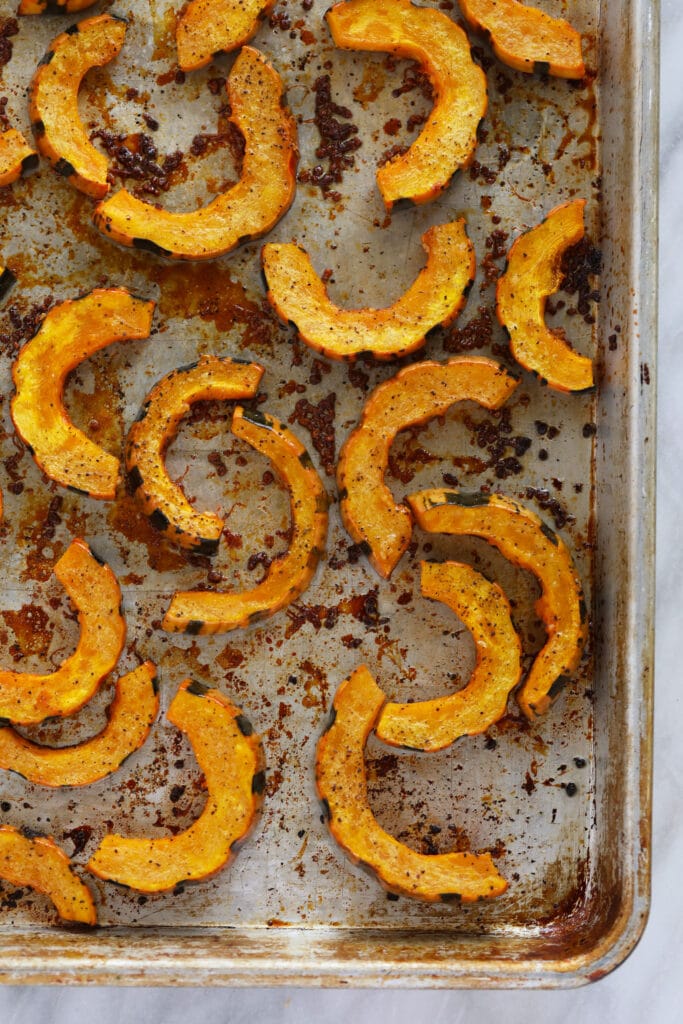 This Easy Roasted Delicata Squash is the perfect pairing to any harvest meal! Enjoy a creme fresh drizzle and the rich savory flavors of delicata squash. No peeling required! roasted delicata squash on a roasting pan