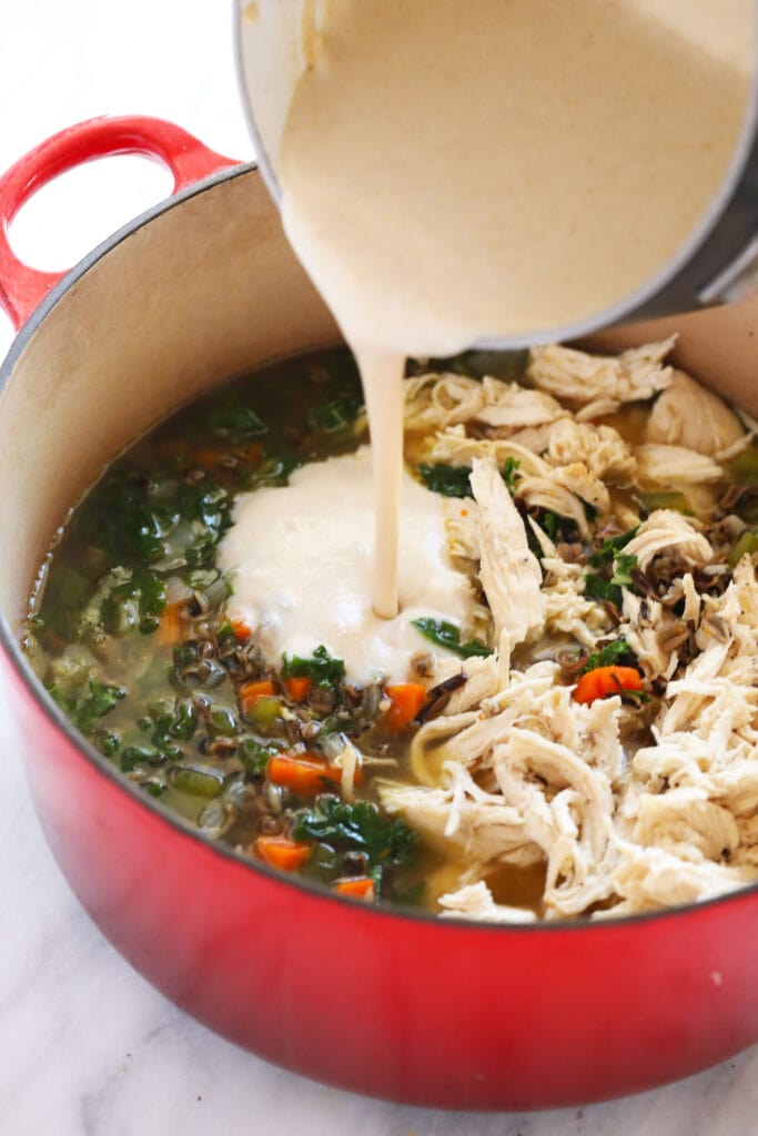 This cozy stovetop Chicken Wild Rice Soup is packed with healthy veggies and made creamy with a delicious roux. Make a large batch and enjoy it throughout the week! roux being poured into chicken wild rice soup to make it creamy
