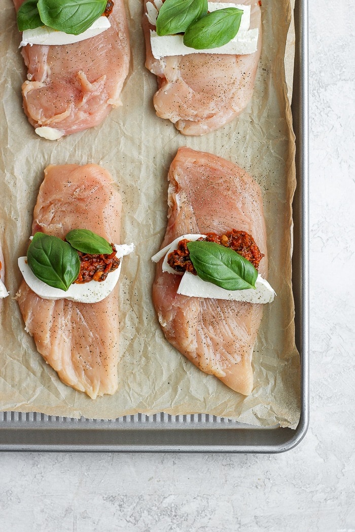 This Caprese Stuffed Chicken Breast Recipe is an easy, healthy dinner that will wow your dinner guests. With only a few ingredients and easy step-by-step instructions, you'll have this delicious dinner ready in under 60 minutes. Enjoy! Caprese stuffed chicken breast on a baking tray