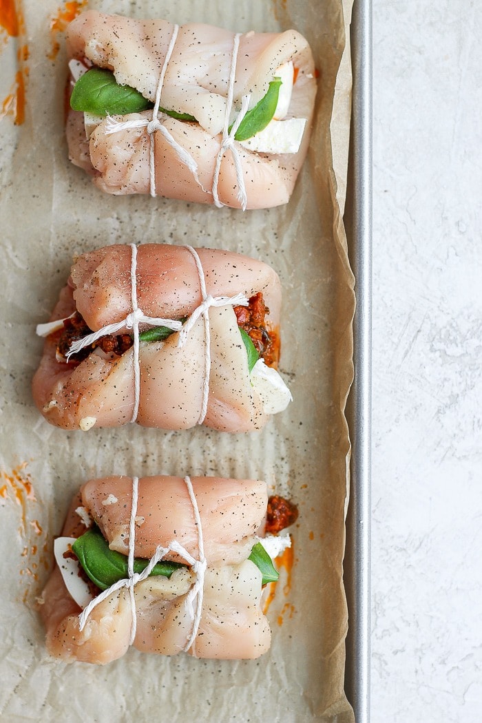 This Caprese Stuffed Chicken Breast Recipe is an easy, healthy dinner that will wow your dinner guests. With only a few ingredients and easy step-by-step instructions, you'll have this delicious dinner ready in under 60 minutes. Enjoy! Caprese stuffed chicken breast rolled up on a baking tray