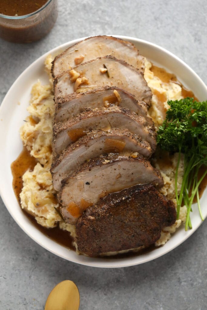 This is the most tender Slow Cooker Pork Loin roast recipe ever! It's served with potatoes and a savory gravy for the perfect meal. Enjoy! slow cooker pork loin on a bed of mashed potatoes covered in delicious homemade gravy