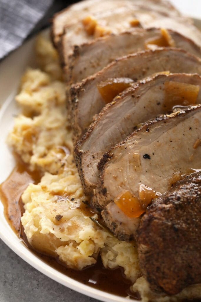 This is the most tender Slow Cooker Pork Loin roast recipe ever! It's served with potatoes and a savory gravy for the perfect meal. Enjoy! slow cooker pork loin sliced and looking delicious covered in gravy