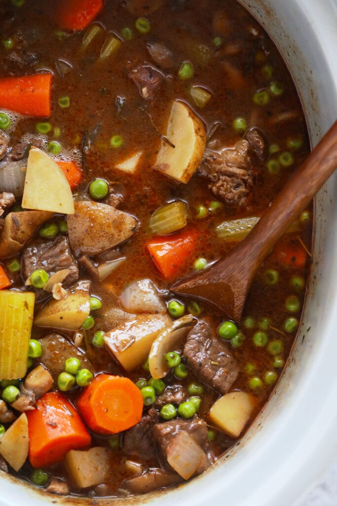 This is the most tender and flavorful Slow Cooker Beef Stew you'll ever have! Fall apart beef and tons of veggies make this beef stew the perfect (and healthy!) cozy comfort meal. beef stew in the slow cooker being stirred with a spoon
