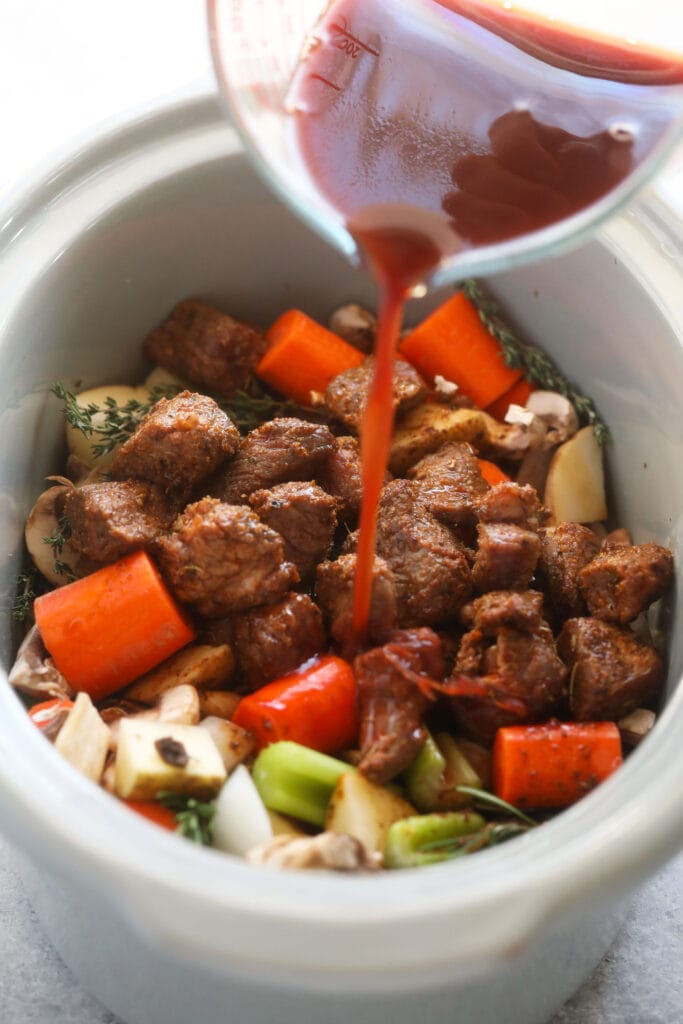 This is the most tender and flavorful Slow Cooker Beef Stew you'll ever have! Fall apart beef and tons of veggies make this beef stew the perfect (and healthy!) cozy comfort meal. slow cooker beef stew ingredients being mixed together in a slow cooker