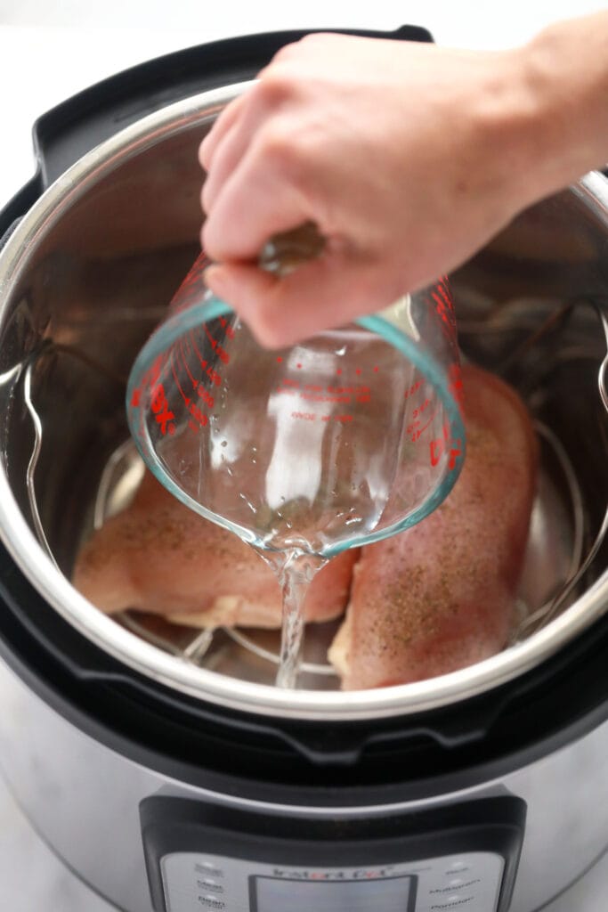 Wondering how to make shredded chicken in the Instant Pot? Look no further! This easy Instant Pot Shredded Chicken recipe is ready in less than 20 minutes, and will easily become a meal-prep staple in your home. water being poured in the instant pot for instant pot shredded chicken