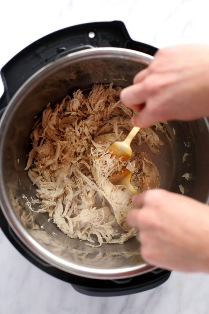 Wondering how to make shredded chicken in the Instant Pot? Look no further! This easy Instant Pot Shredded Chicken recipe is ready in less than 20 minutes, and will easily become a meal-prep staple in your home. two forks shredding instant pot chicken breasts into shredded chicken