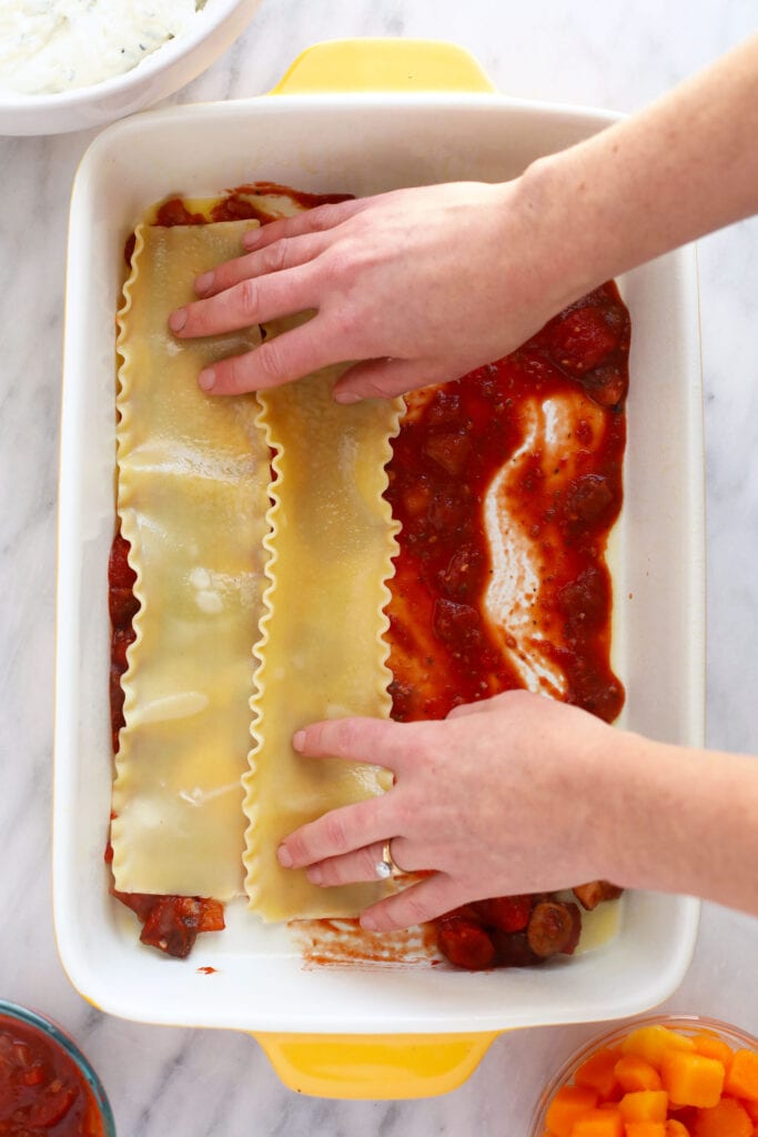 Hands placing lasagna noodles in a 9x13 casserole dish.