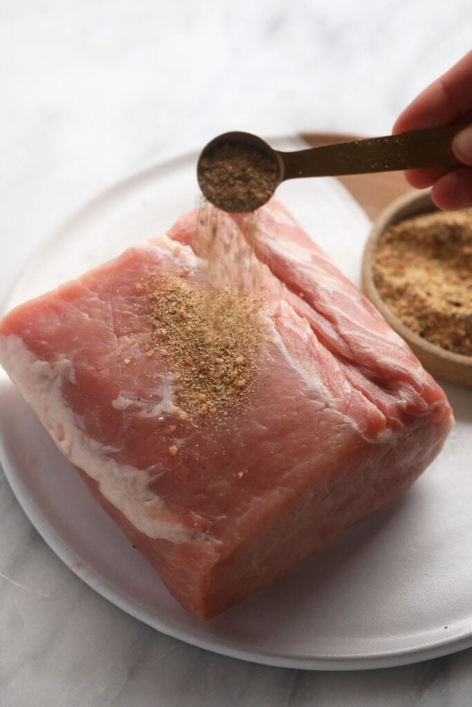 This is the most tender Slow Cooker Pork Loin roast recipe ever! It's served with potatoes and a savory gravy for the perfect meal. Enjoy! raw pork loin roast being seasoned with a pork dry rub