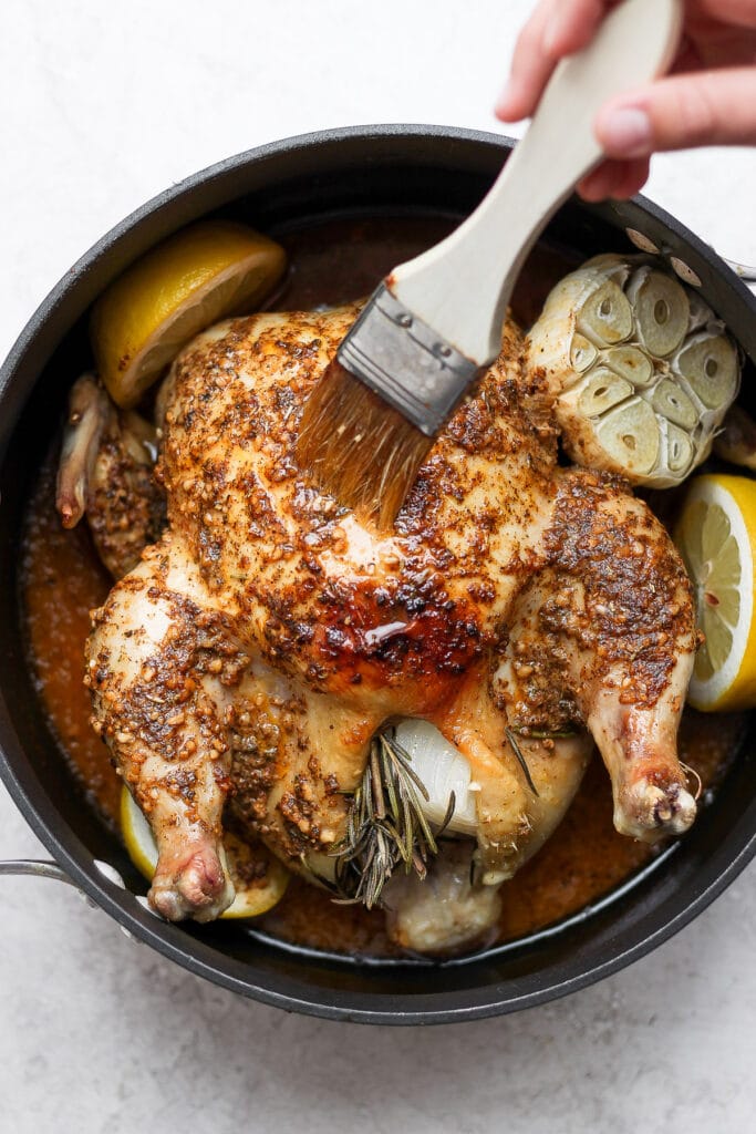 A delicious herby whole roasted chicken recipe made with a whole head of garlic and lemon is the perfect weeknight meal that the whole family will love. brush basting chicken