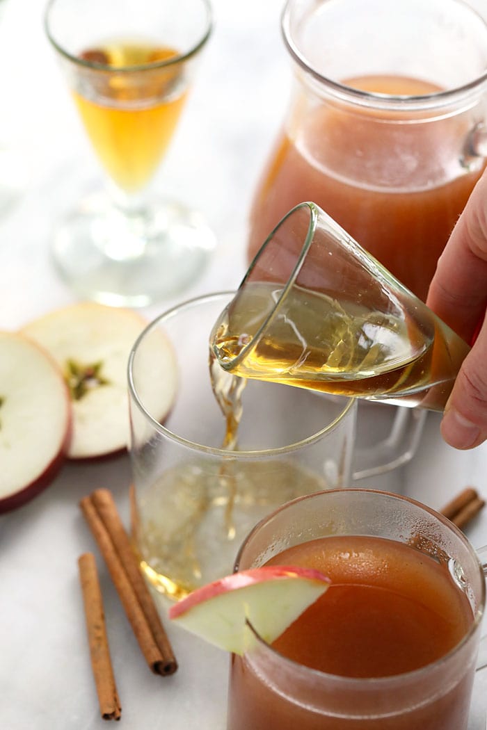 This Spiked Apple Cider is a boozy twist on our traditional apple cider recipe that's been a Fall favorite for years. Make a large batch to serve a crowd, or pour a single serve spiked cider tonight. Cheers! shot of booze being poured in a mug for spiked apple cider
