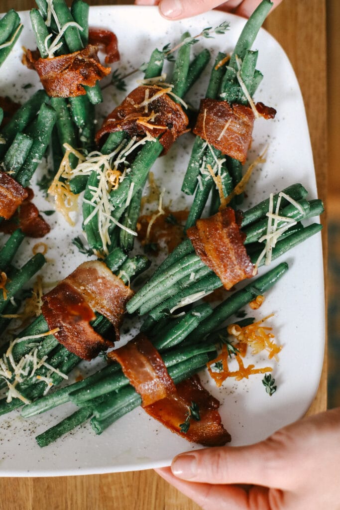 These Bacon Wrapped Green Beans are the perfect holiday appetizer or side! Easy to make and ready in under 30 minutes -- what's not to love?! bacon wrapped green beans on a plate topped with parmesan cheese