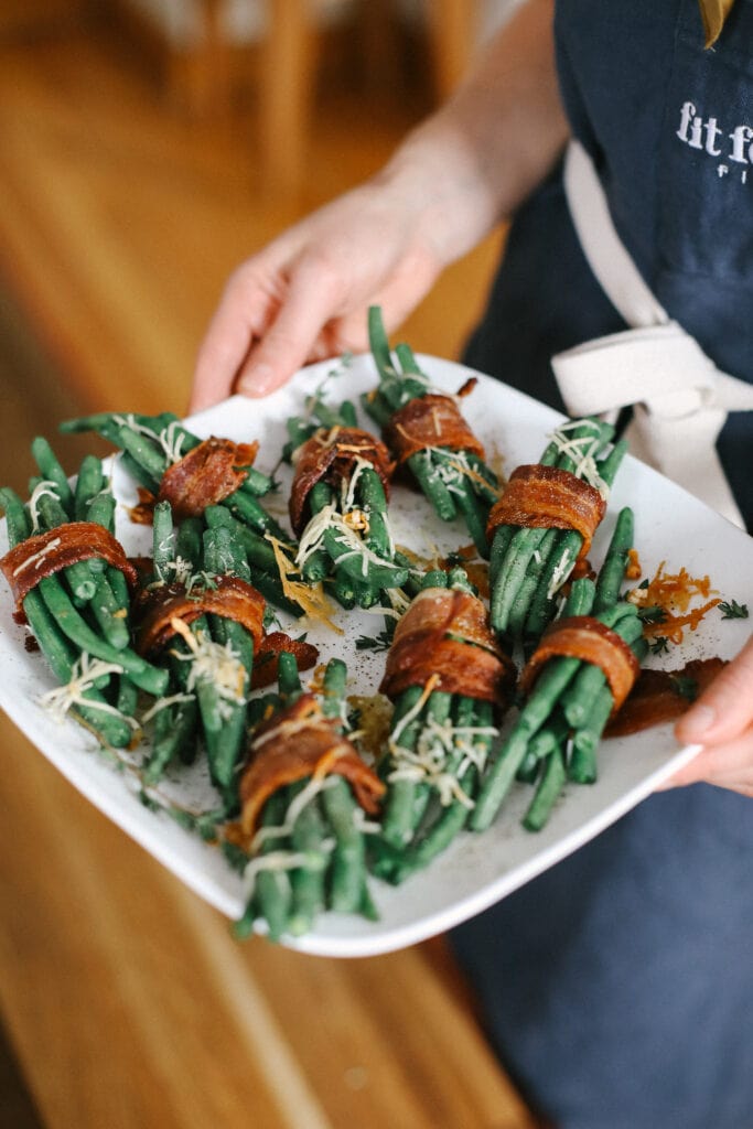 These Bacon Wrapped Green Beans are the perfect holiday appetizer or side! Easy to make and ready in under 30 minutes -- what's not to love?! bacon wrapped green beans on a plate ready to be served