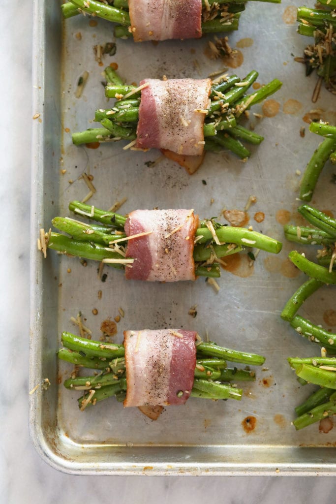 These Bacon Wrapped Green Beans are the perfect holiday appetizer or side! Easy to make and ready in under 30 minutes -- what's not to love?! bacon wrapped green beans ready to be baked on a baking sheet