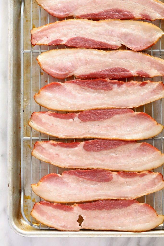 These Bacon Wrapped Green Beans are the perfect holiday appetizer or side! Easy to make and ready in under 30 minutes -- what's not to love?! raw bacon ready to be baked