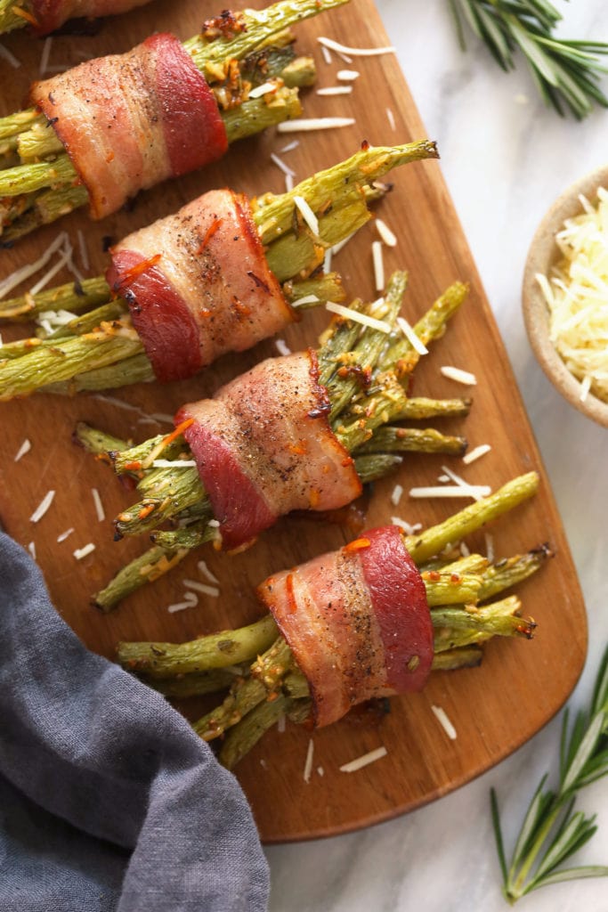 These Bacon Wrapped Green Beans are the perfect holiday appetizer or side! Easy to make and ready in under 30 minutes -- what's not to love?! bacon wrapped green beans served on a wooden platter