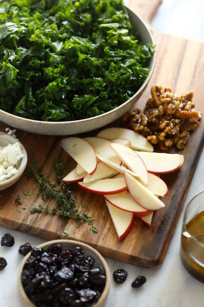 Looking for a last-minute Thanksgiving salad idea? Try our delicious massaged kale, apple, and walnut salad made with goat cheese, dried cherries, and our favorite vinaigrette! ingredients on cutting board