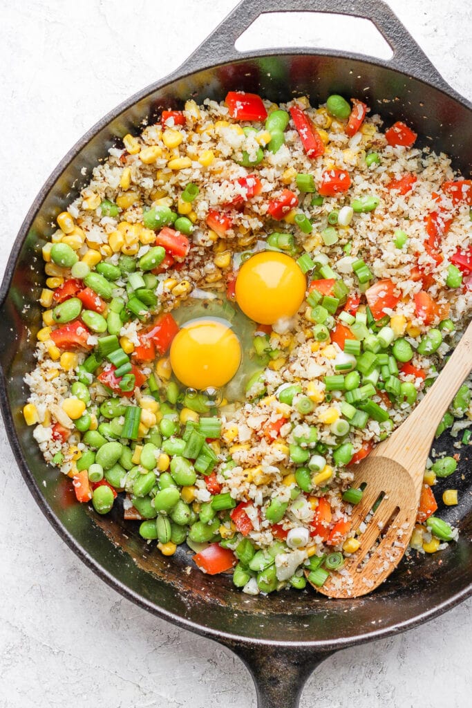 This Cauliflower Fried Rice recipe is a delicious low carb alternative to traditional fried rice. Packed with veggies and a super flavorful sauce, plus it's easy to make. Enjoy! cauliflower fried rice with 2 eggs cracked in the middle of the skillet