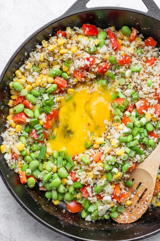 This Cauliflower Fried Rice recipe is a delicious low carb alternative to traditional fried rice. Packed with veggies and a super flavorful sauce, plus it's easy to make. Enjoy! cauliflower fried rice with eggs scrambled in the middle of the skillet