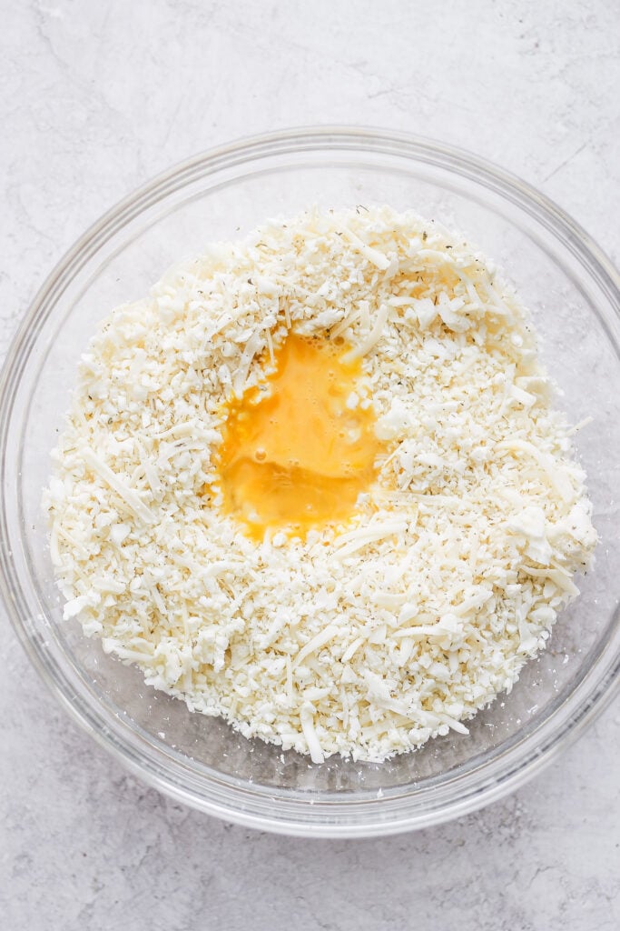 Cauliflower rice in a bowl with cheese and a whisked egg.