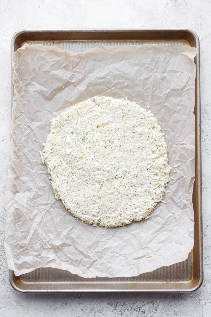 Cauliflower pizza crust made into a circle on a baking sheet.
