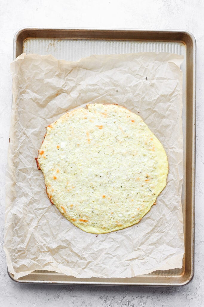 Baked cauliflower pizza crust on parchment paper.