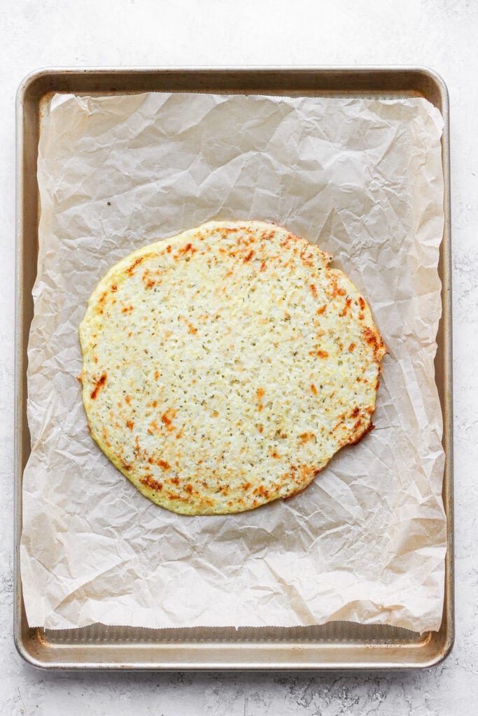 Golden cauliflower pizza crust on parchment paper.