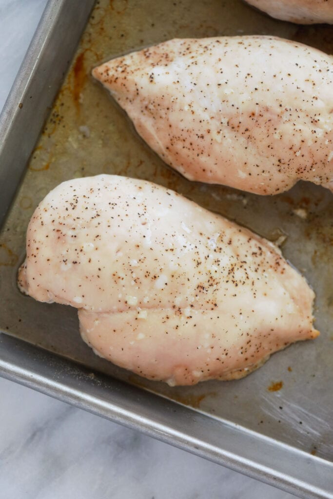 Wondering how to make the easiest shredded chicken? Look no further! This shredded chicken is baked to perfection, and will easily become a meal-prep staple in your home. chicken breast on a baking sheet