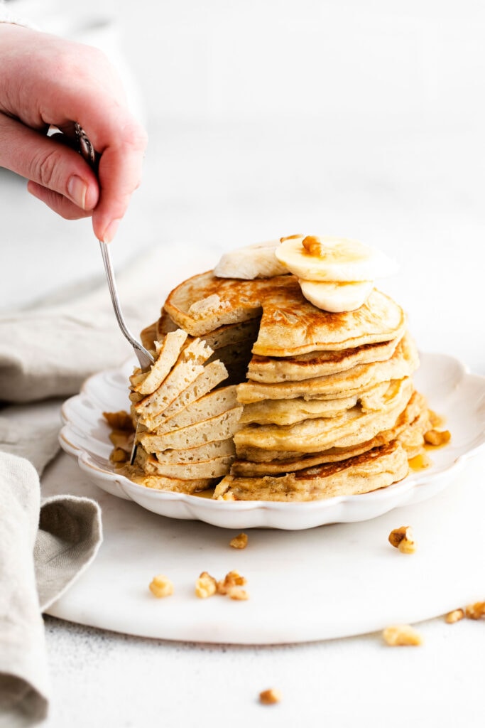 This banana pancake recipe is the ultimate weekend breakfast. Why? These banana pancakes come out super fluffy and they taste heavenly topped with fresh banana and warm maple syrup. forking stack of pancakes