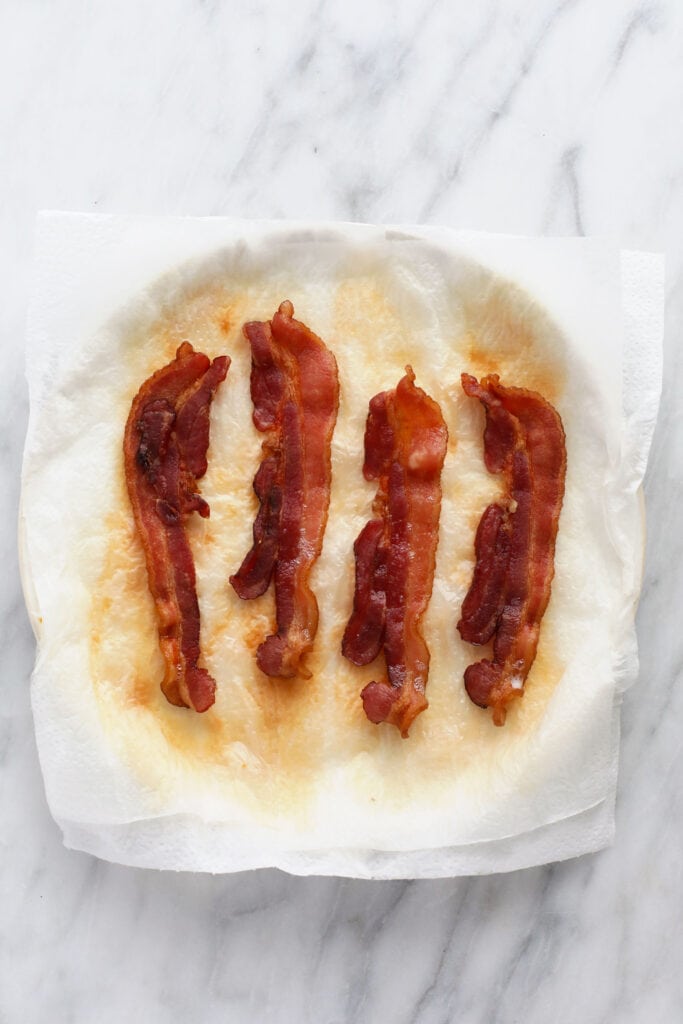 Cooked bacon on a plate that is covered in paper towel.