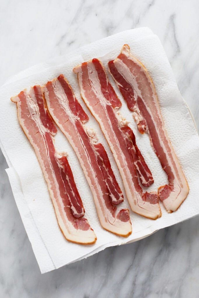 Raw bacon on a plate on top of paper towel.